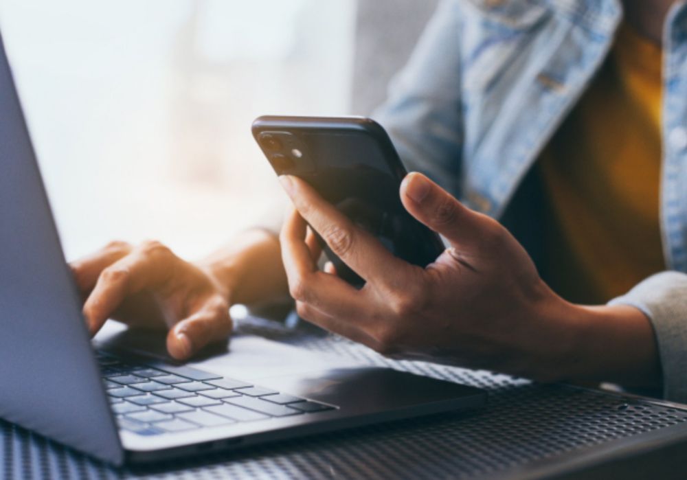 Woman typing on a laptop and holding a mobile with her hand 