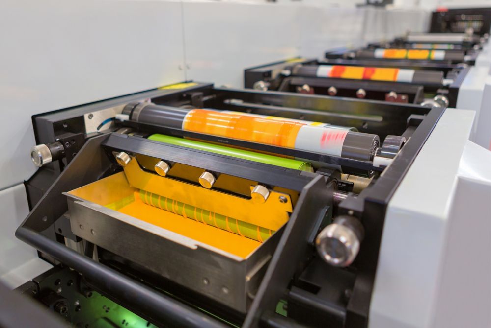 A row of inked printing press rollers, each coated with a different hue of orange.  