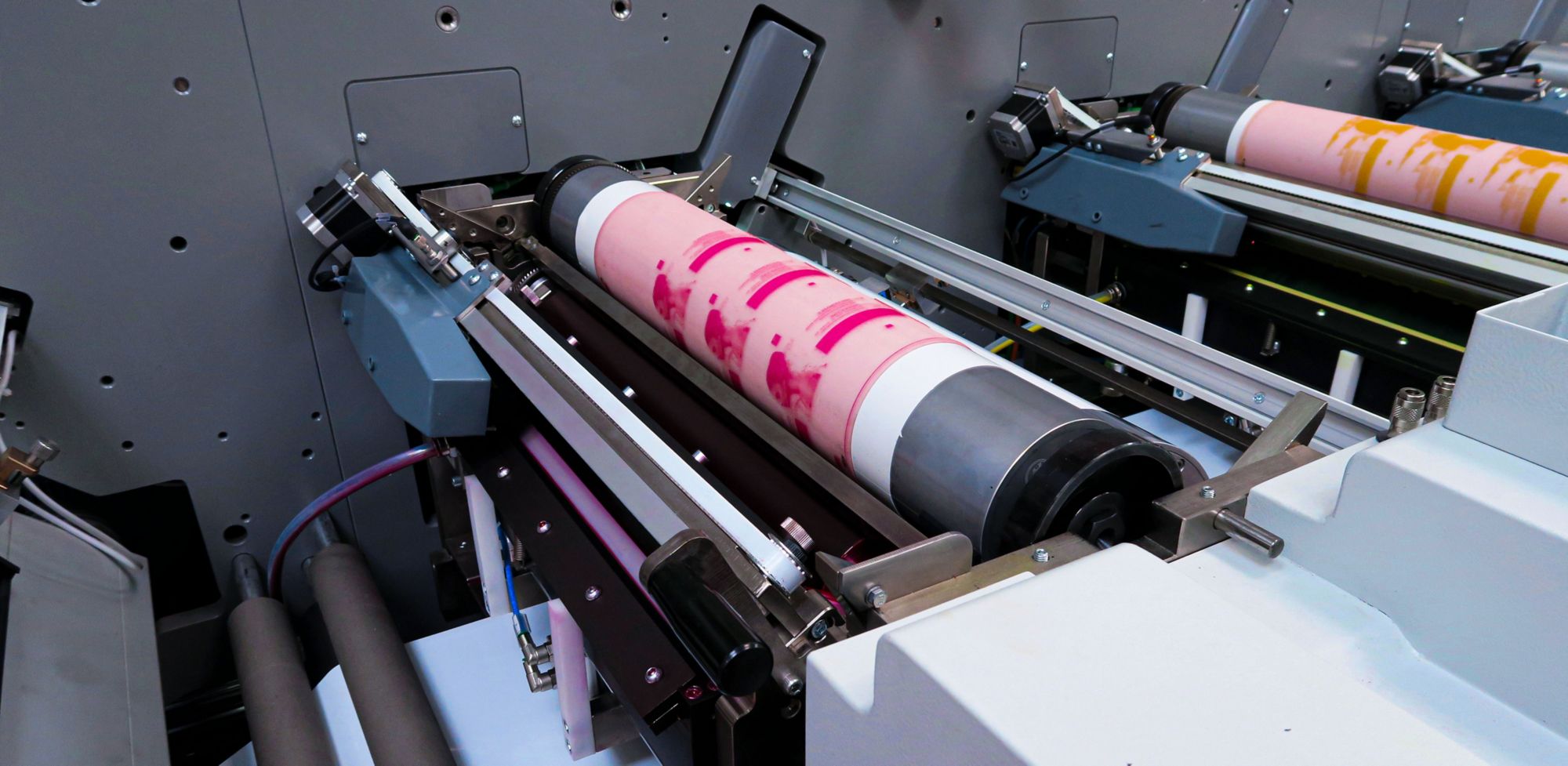 Two roller printing machines, one printing with dark pink ink and the other with yellow ink. 