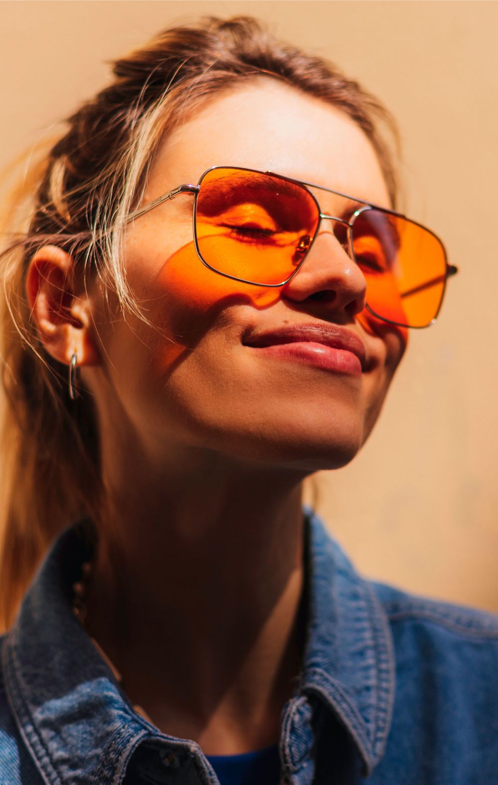 A woman smiles wearing orange-tinted aviator sunglasses. 