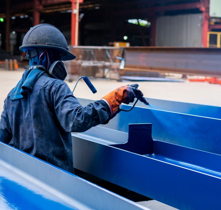 A person sprays protective coating on metal. 