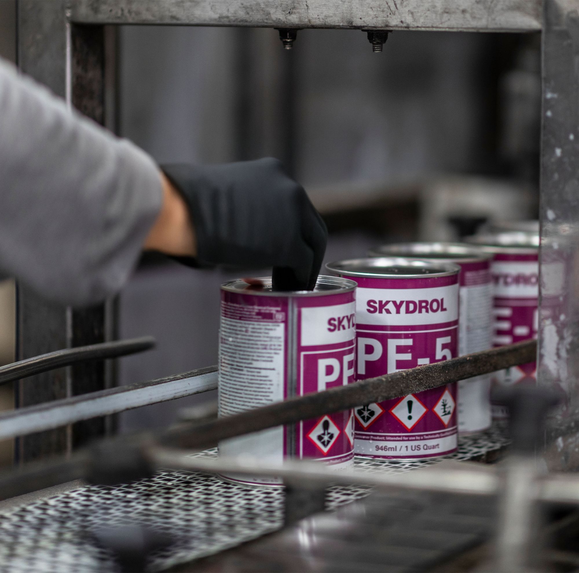 A gloved person handles Skydrol cans on the production line. 