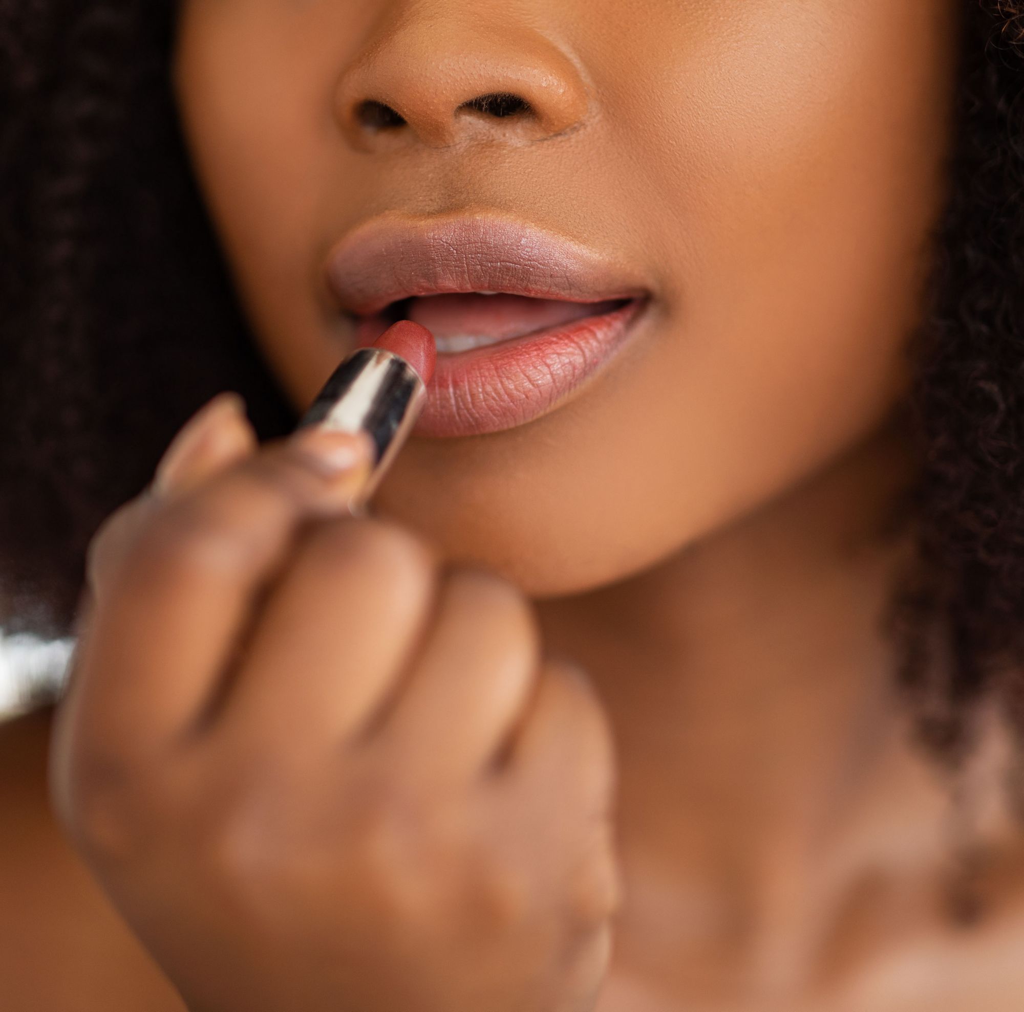 A close-up of a woman carefully applying red lipstick to her lips. 