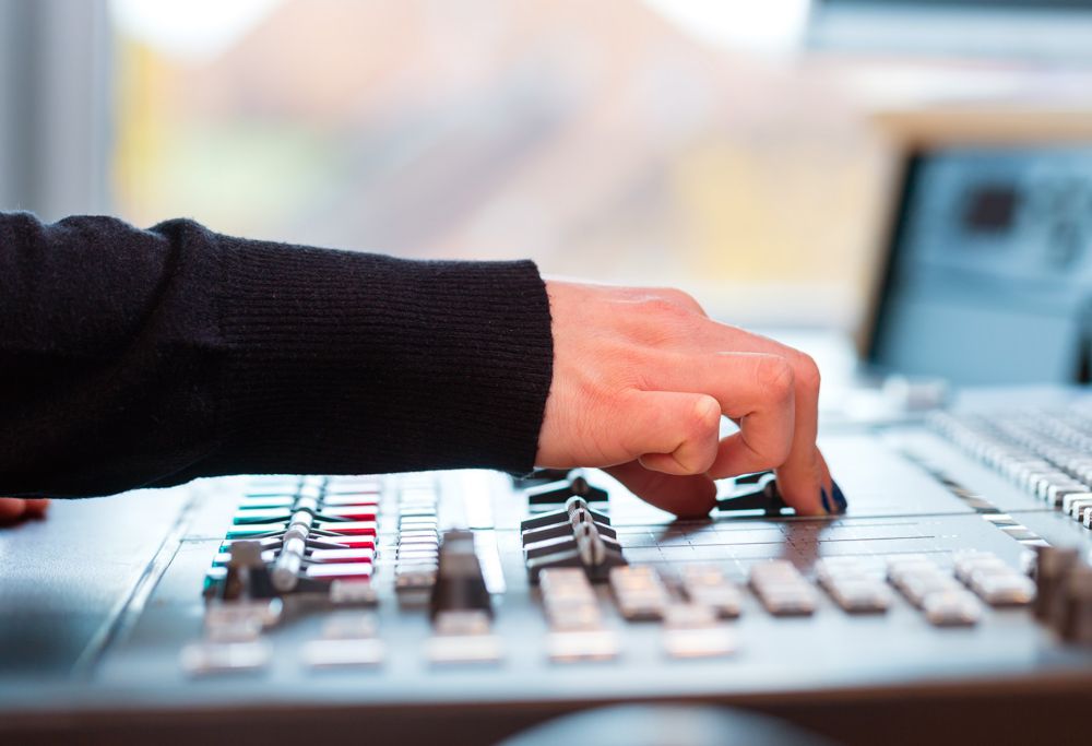 A person adjusting a audio mixing console. 