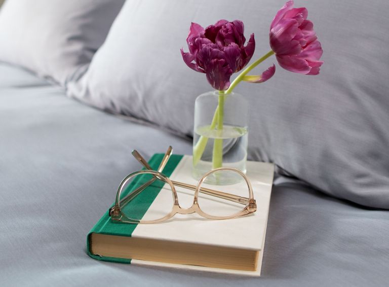 Tritan glasses and flowers placed on top of a book sitting on a bed. 