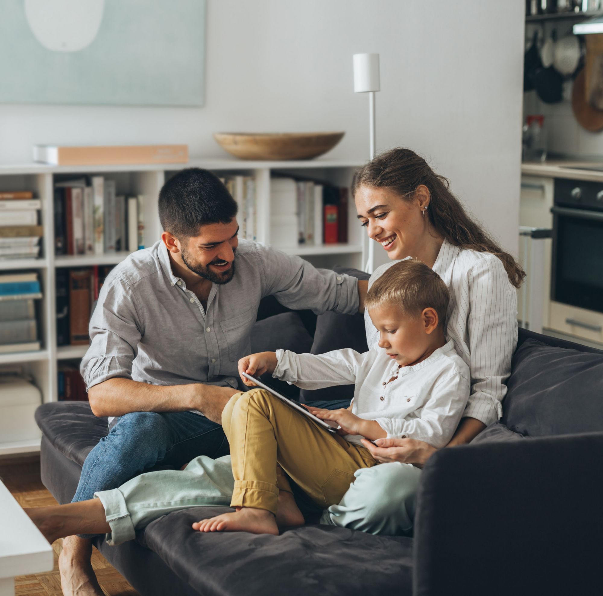 Two parents read with their child on a living room couch. 