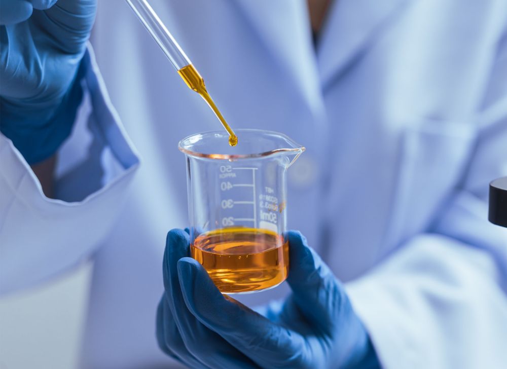 A gloved scientist is pipetting orange liquid into a beaker. 