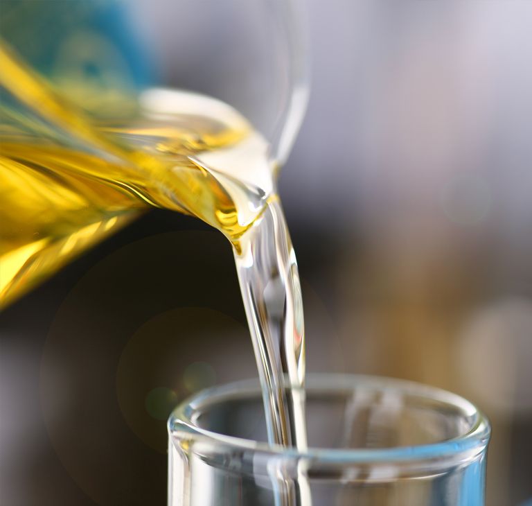 A researcher pours yellow liquid into a smaller beaker. 