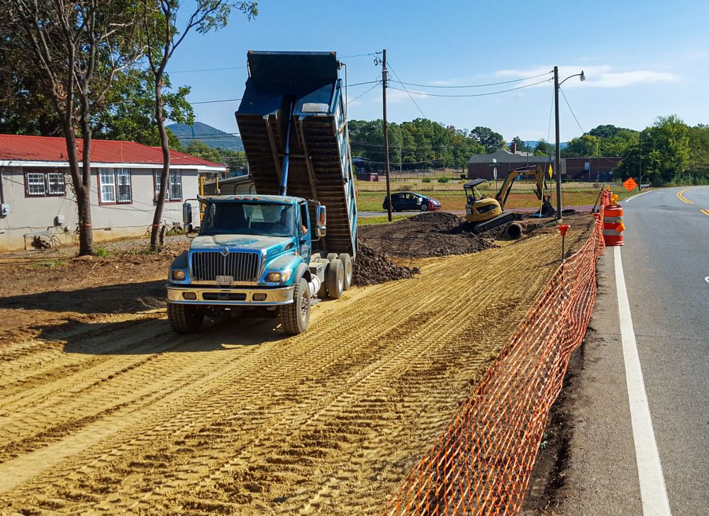A dump truck pours dirt onto a surface.  