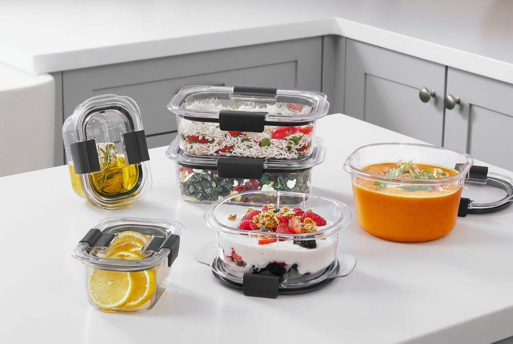 Six Rubbermaid Brilliance food storage containers containing different kinds of food, ranging from soups to fresh fruit. 