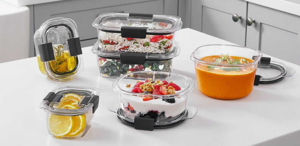 Six Rubbermaid Brilliance food storage containers containing different kinds of food, ranging from soups to fresh fruit. 