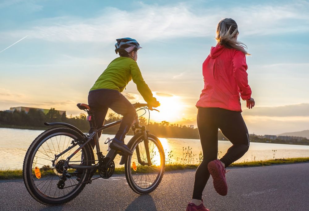 A woman running alongside a boy biking as the sun sets. 