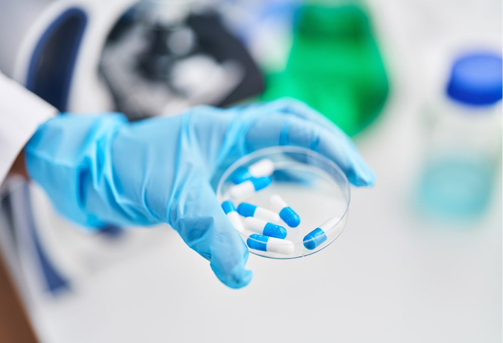 A scientist holding a petri dish containing blue and white pills.  