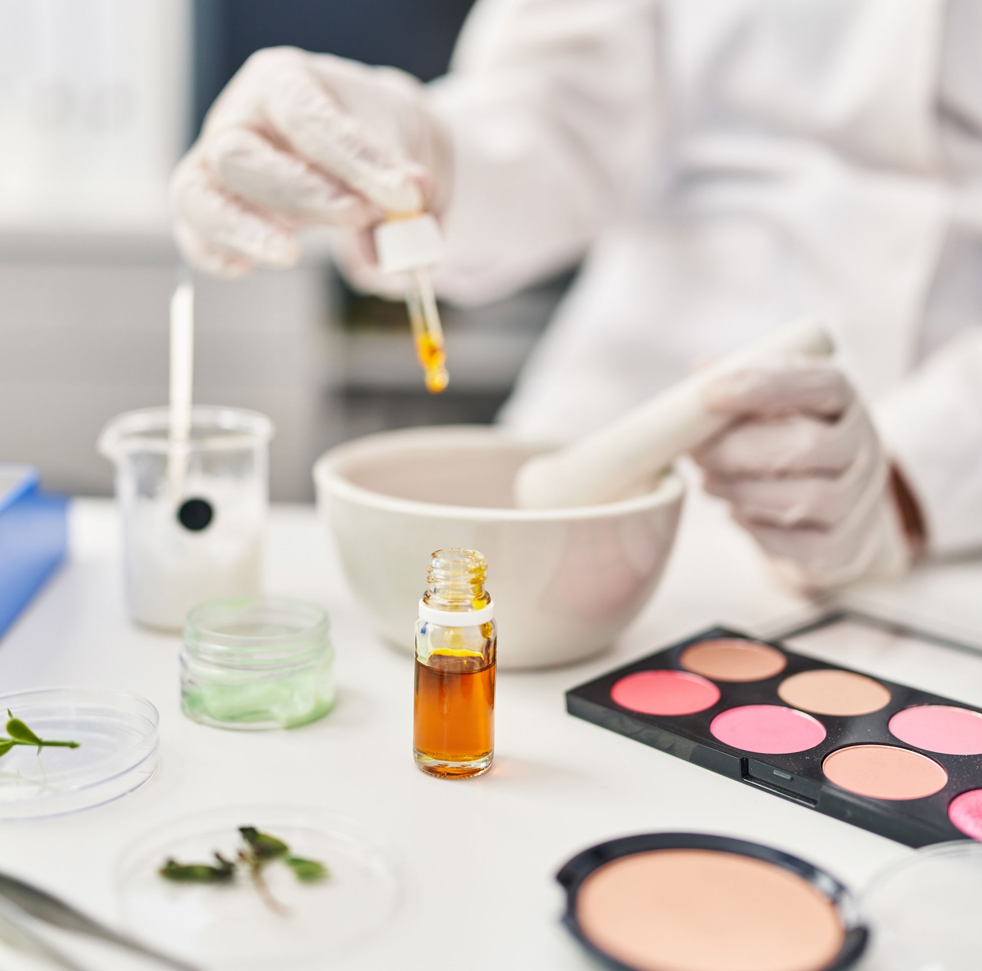 Cosmetics being formulated by a scientist using a dropper bottle of oil, mortar and pestle.   