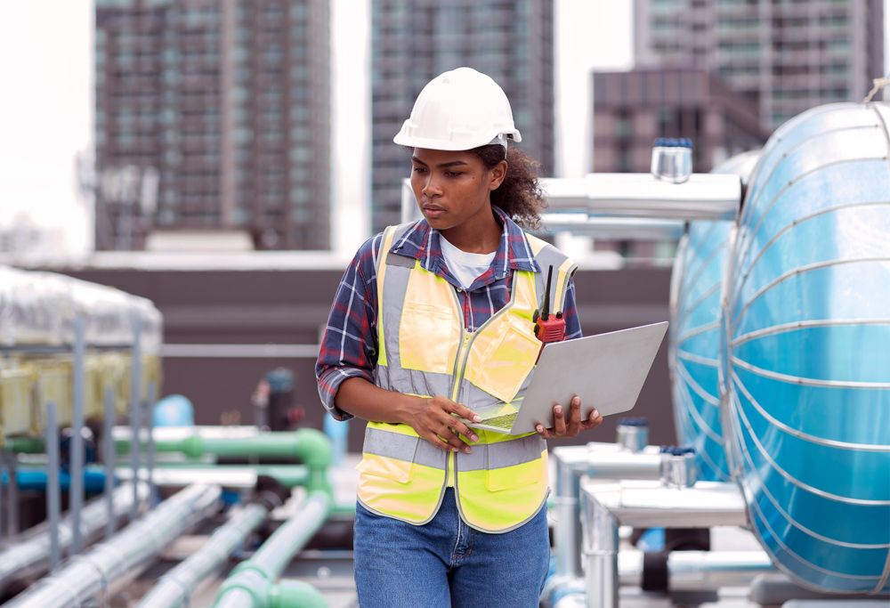 A female site worker inspects something while holding a laptop 