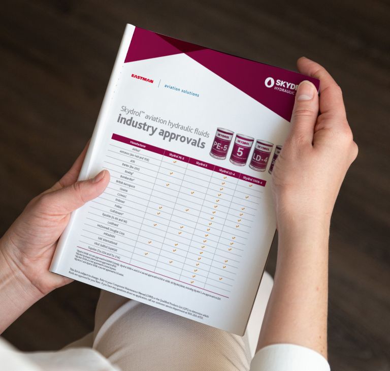 A person holds a sheet listing Skydrol aviation hydraulic fluid industry approvals. 