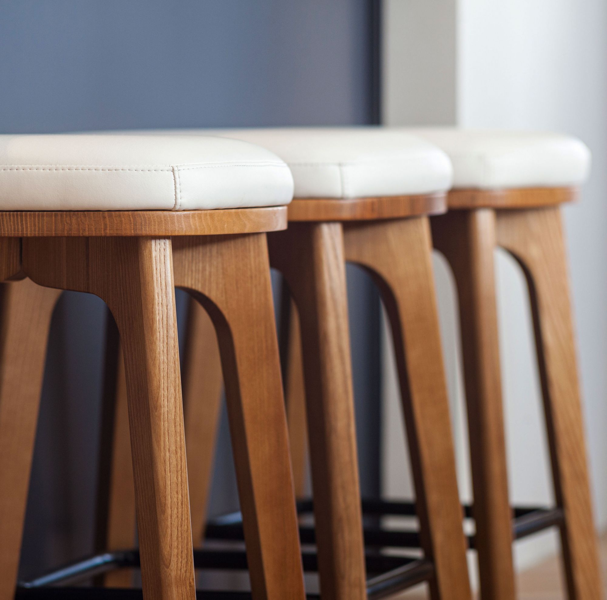 Three white-cushioned wooden stools sit next to a wall. 