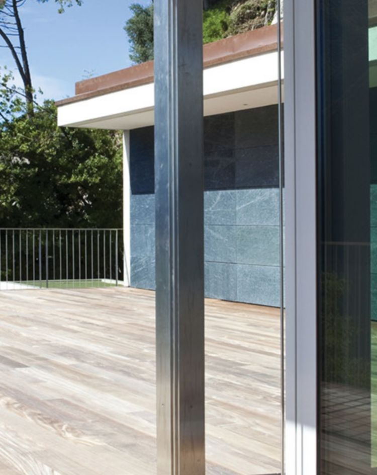 Wooden deck beside a modern glass-walled home with lake views. 