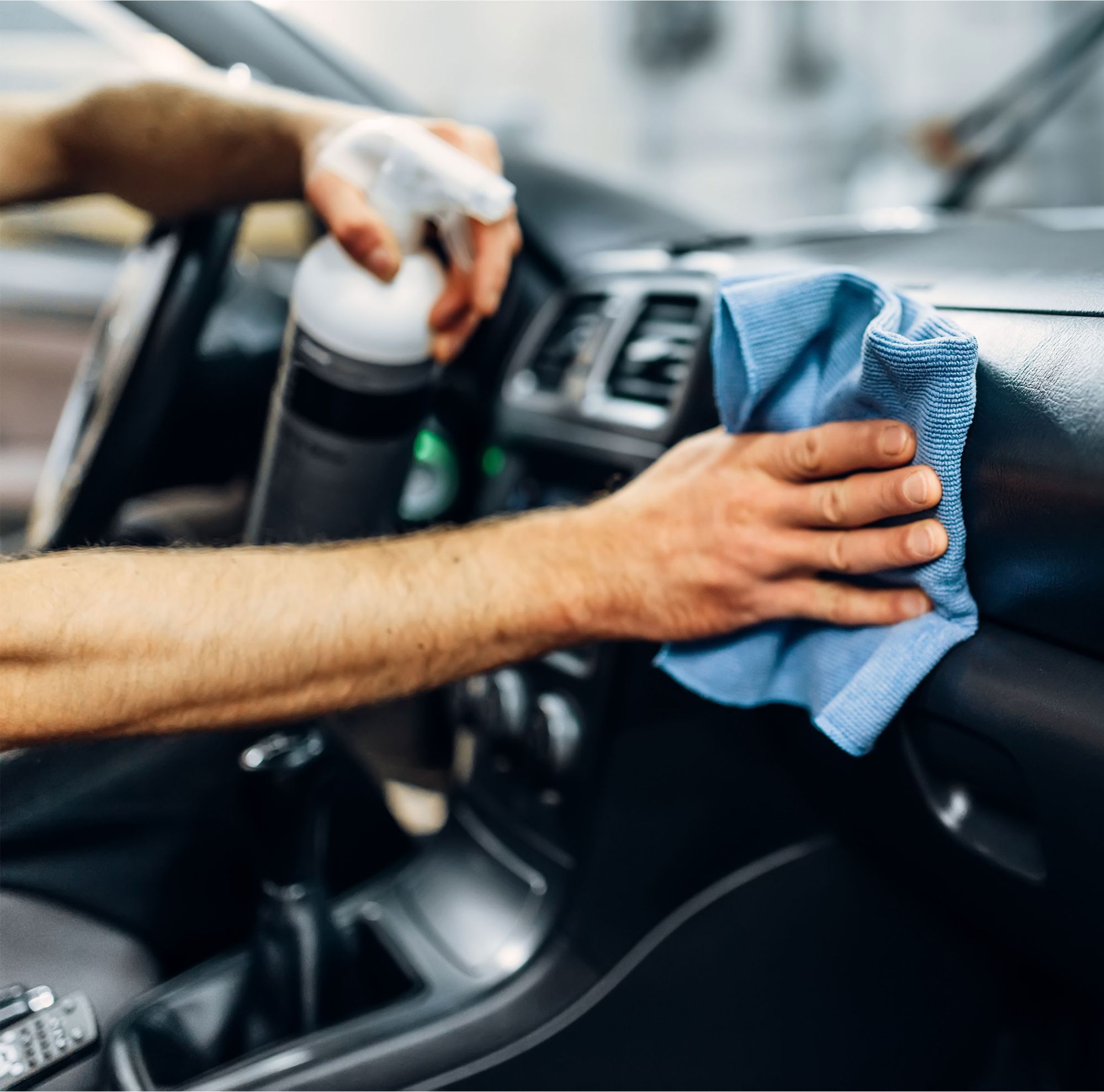 A person cleaning the car dashboard with a blue towel. 