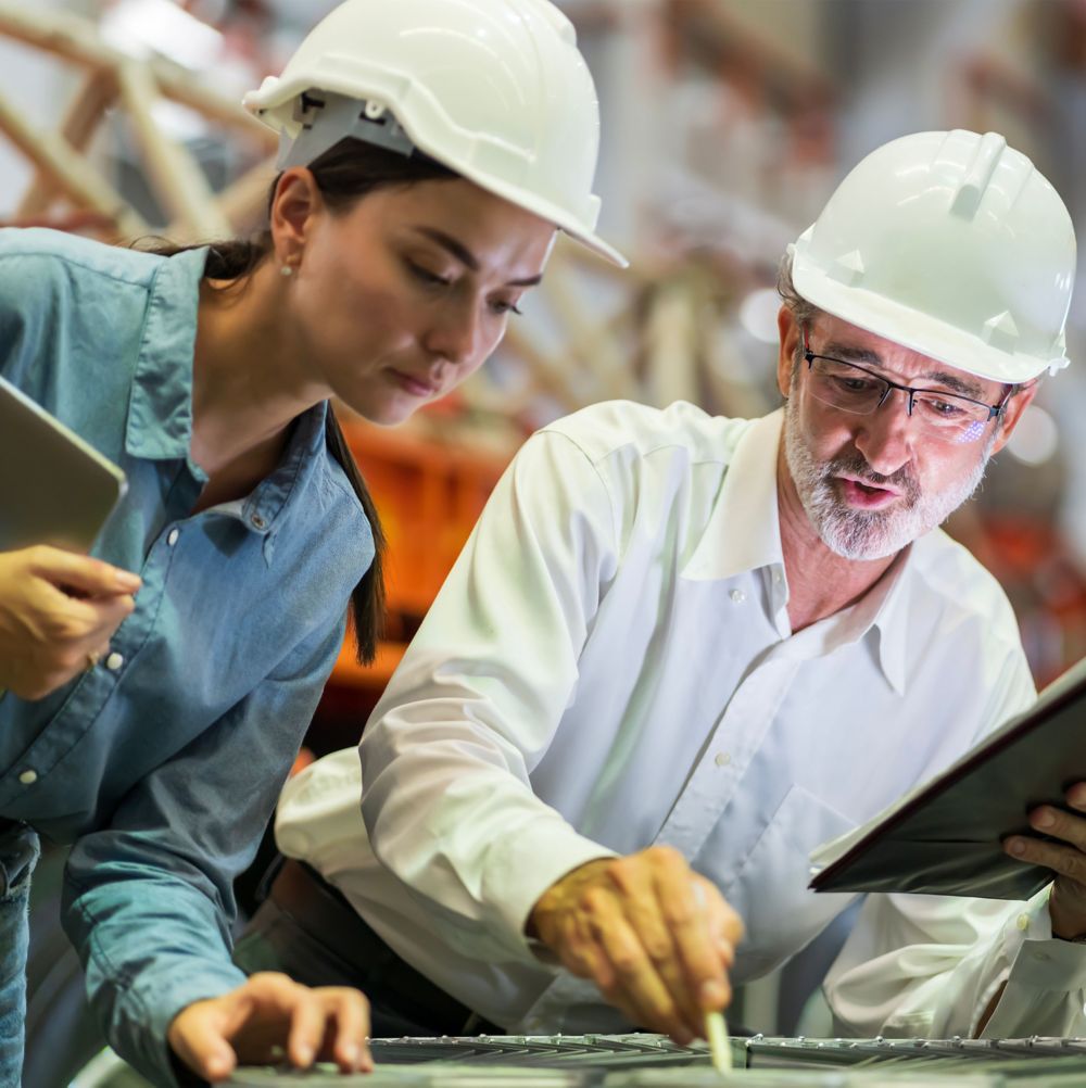 Two employees in hard hats review a start-up plan at a construction site. 