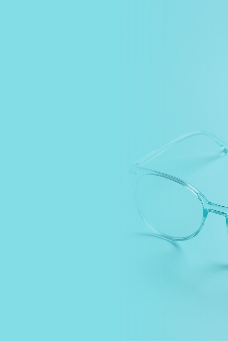 A pair of clear eyeglass resting on a light blue surface. 