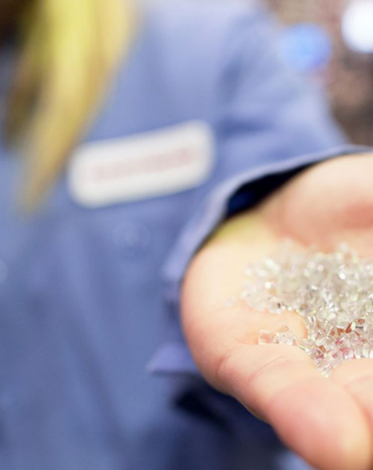 Hand holding a small pile of clear plastic pellets in an industrial setting. 