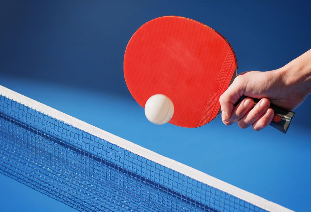 A red table tennis paddle hitting ping pong ball. 