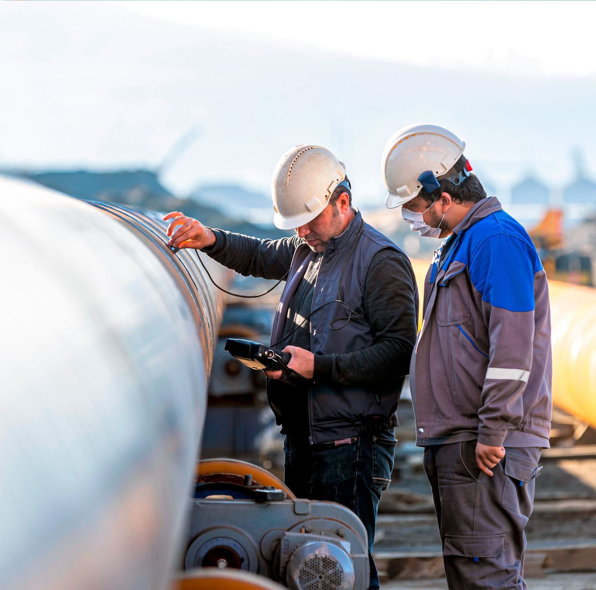 Two engineers in PPE checking pipelines.   