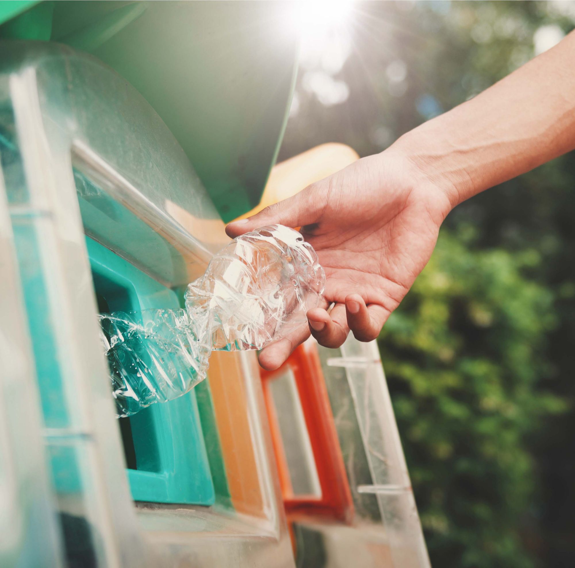 A hand putting a plastic bottle being put into a recycling bin. 