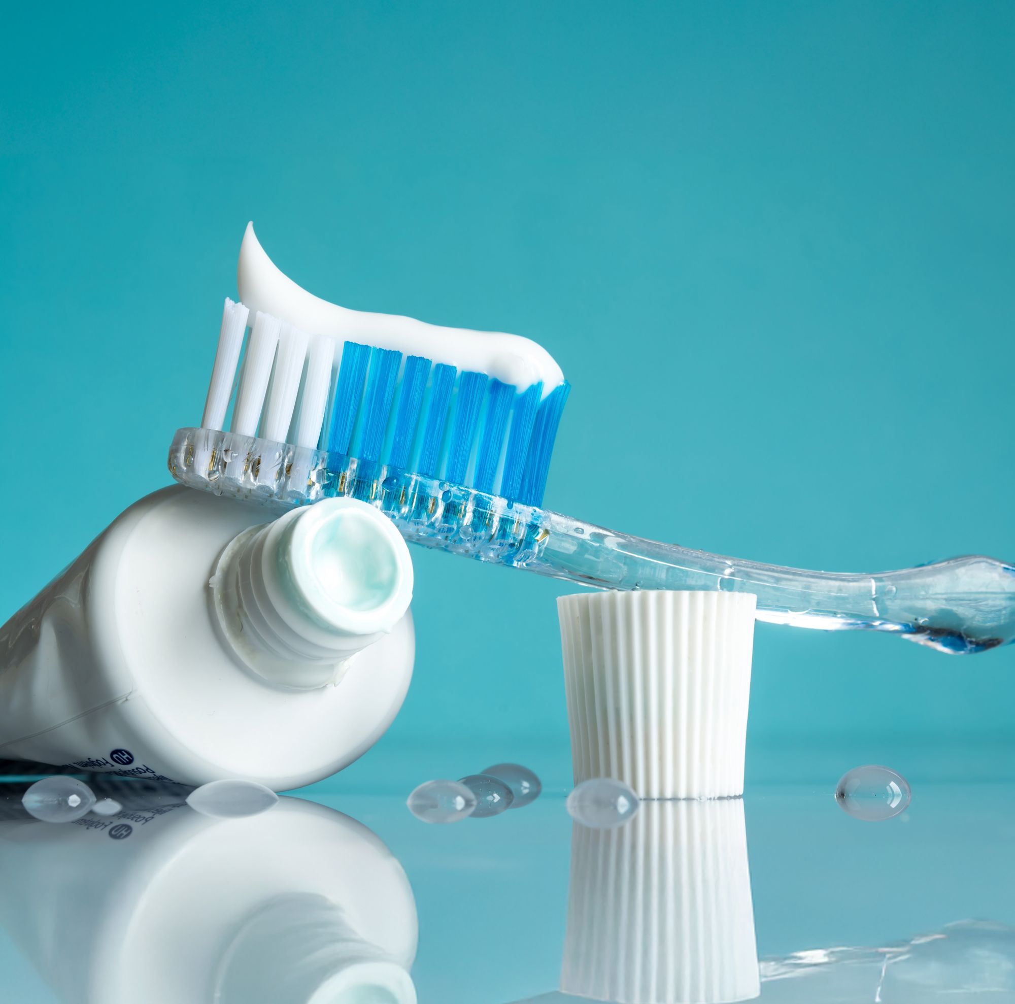 A close-up of a toothbrush with toothpaste on its bristles, resting on an open toothpaste container. 