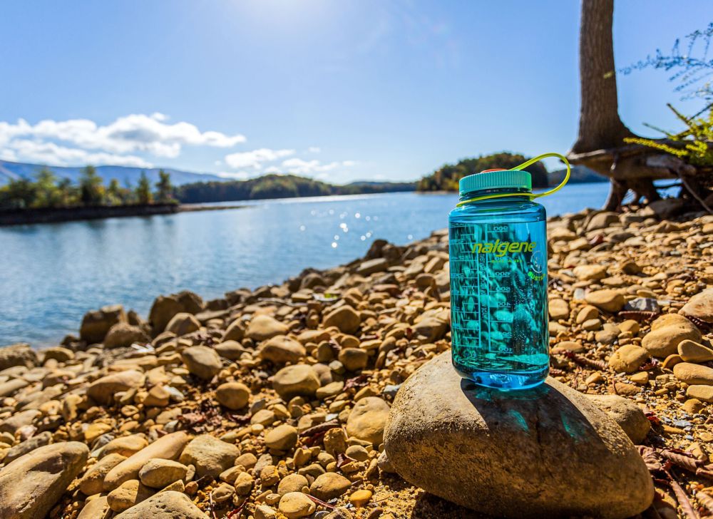 A blue container sits on a rock near a body of water. 