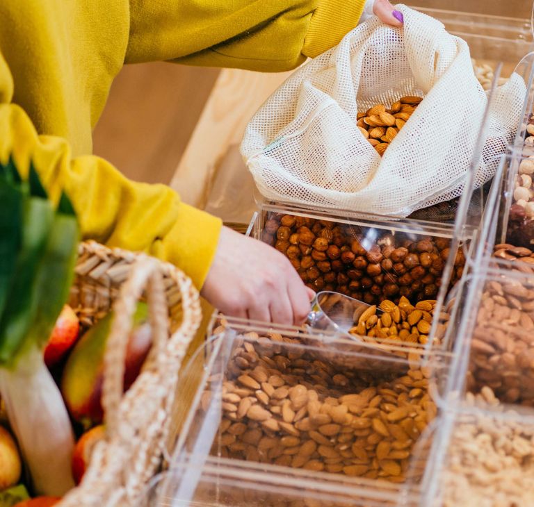 A person scoops almonds into a reusable mesh bag. 