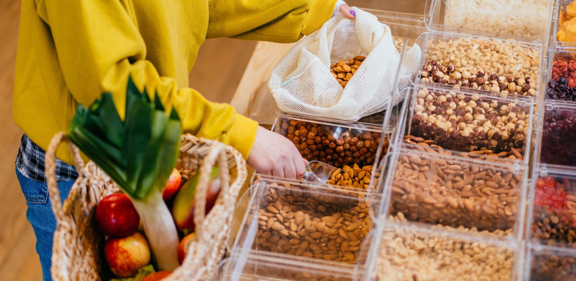 A person scoops almonds into a reusable mesh bag. 