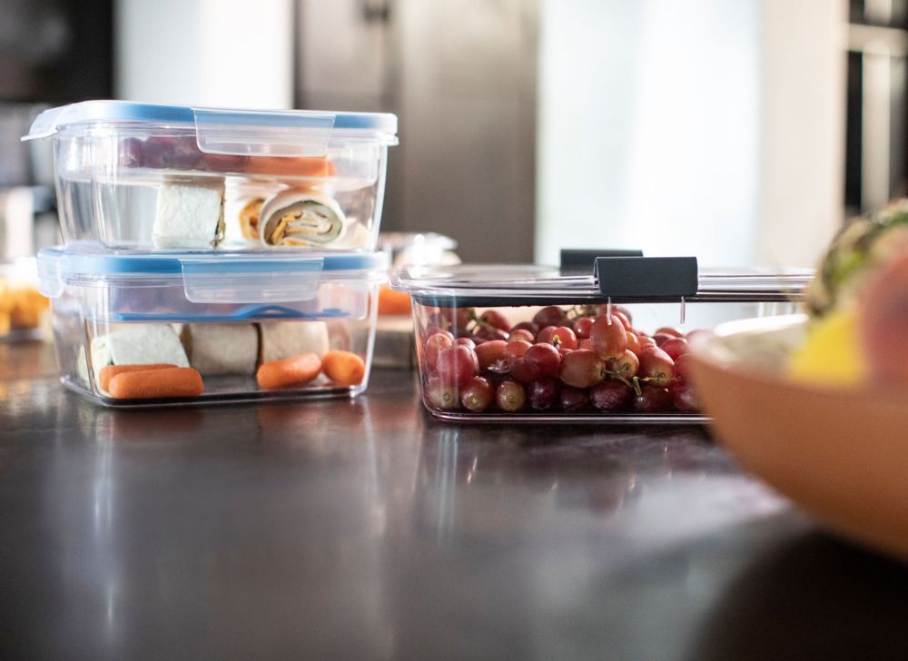 Three clear food storage containers filled with grapes, carrots and wraps.  