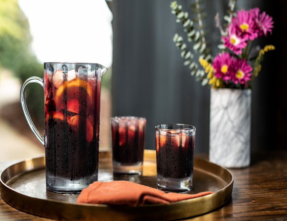 A pitcher and two glasses full of iced beverage sit on a tray atop a wooden surface. 