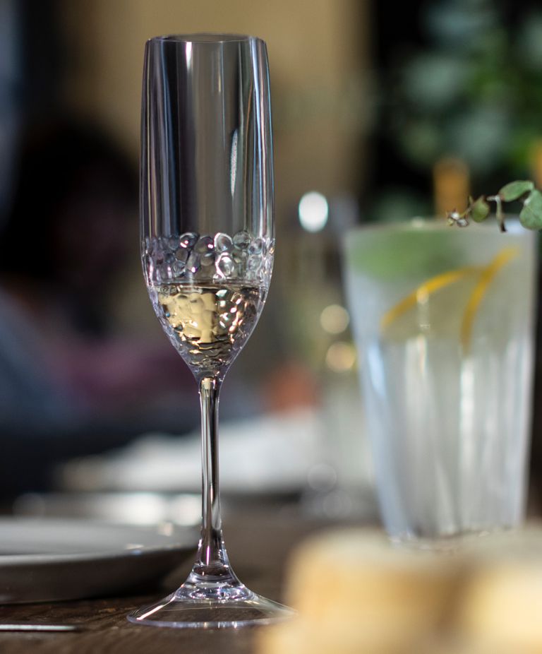 A champagne flute filled with a bit of champagne sits on a wooden table. 