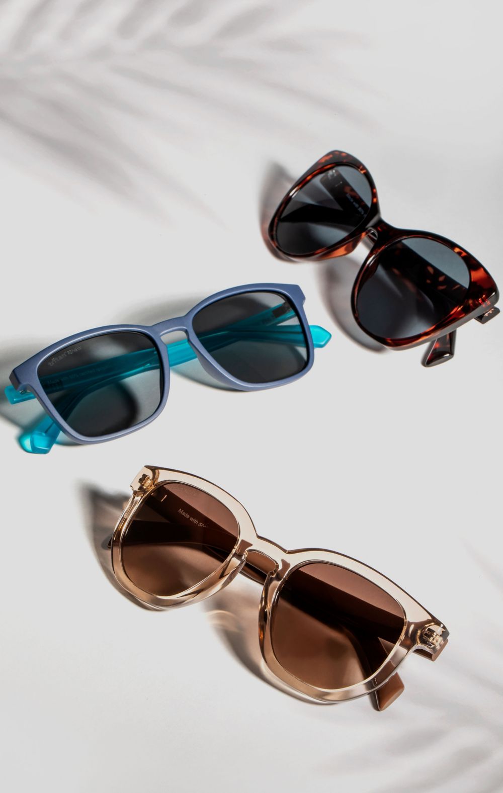 Three sunglasses of varying colors lay on a white surface. 