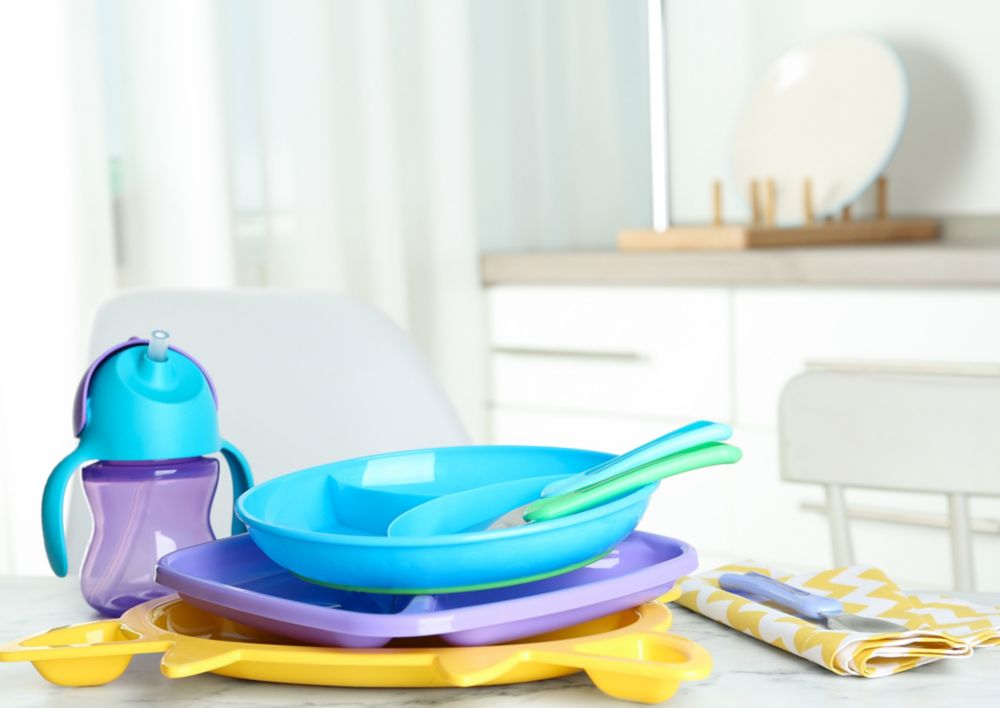 A stack of children’s tableware including a sippy cup, plates and spoons sits on a white table. 