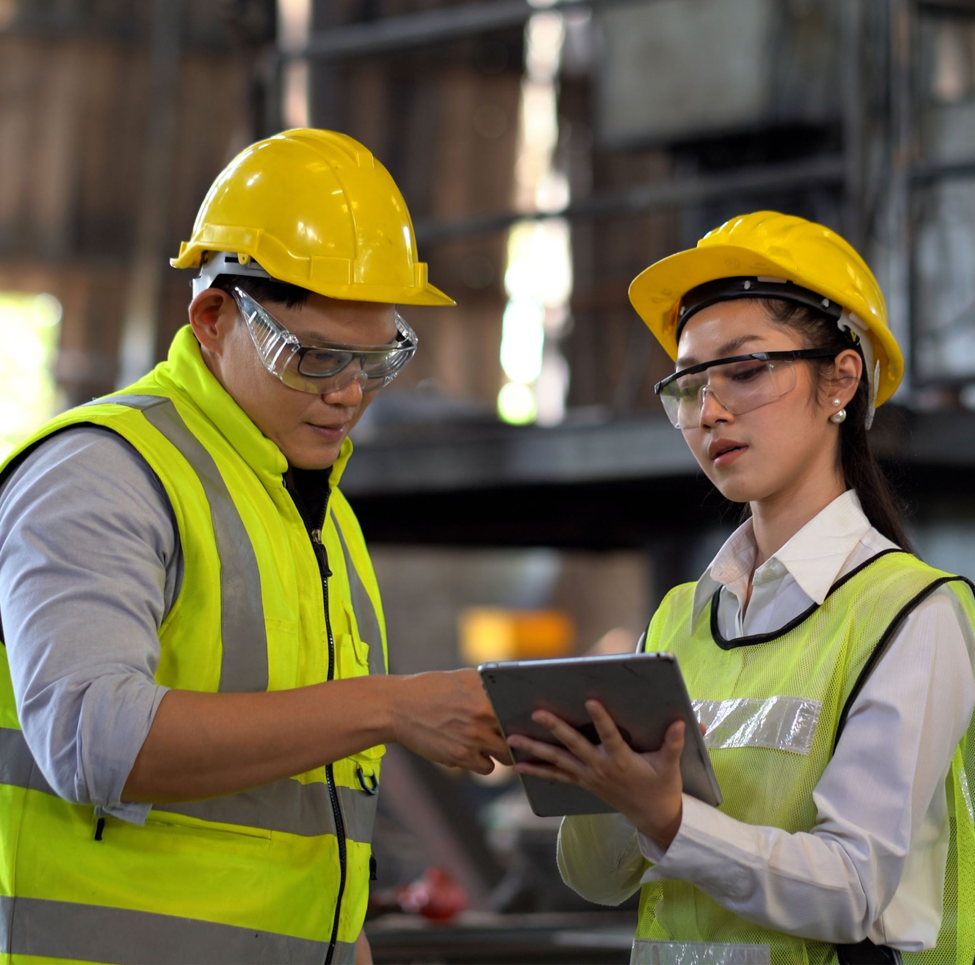 Asian industrial engineers wearing eyeglass and helmet discussing while using a digital tablet in a industry facility. 