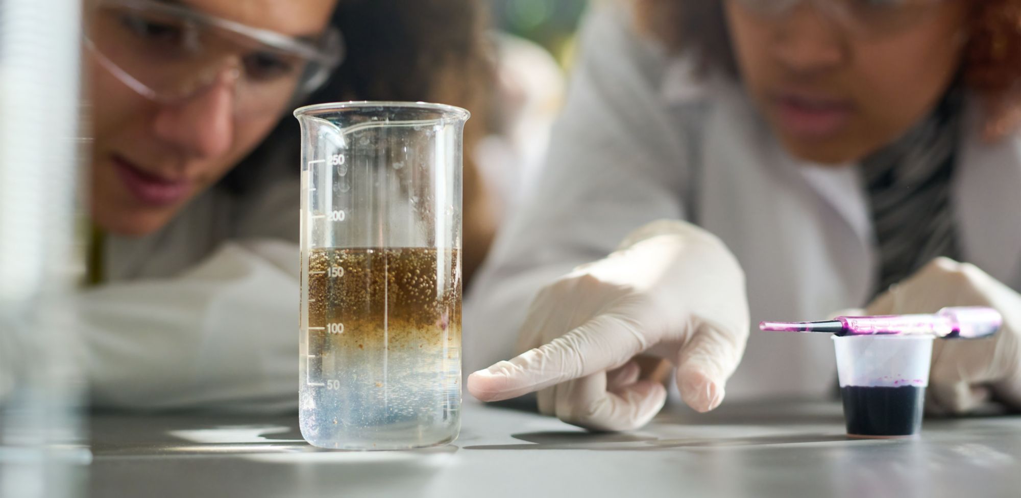 Two people look at a liquid in a vial on a surface.  