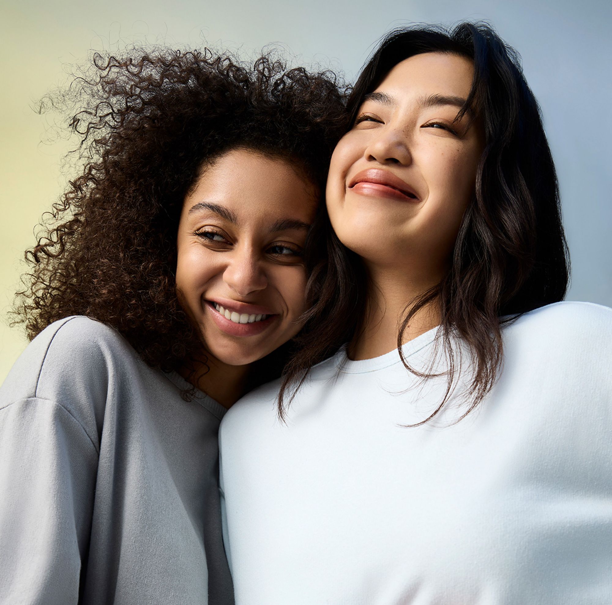 Two smiling people in sweatshirts embrace each other. 