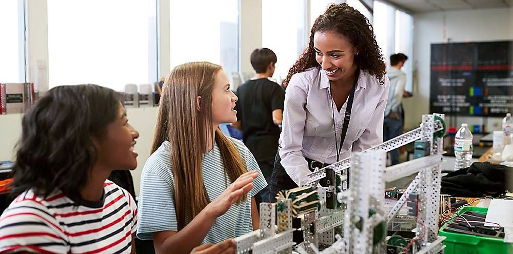 Two students sitting in front of a robotics project, speaking to an instructor about their future careers. 