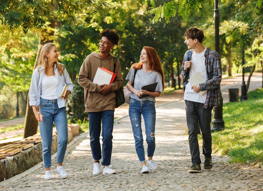 Four university students walk together as they smile at one another. 