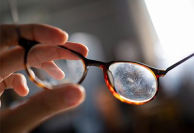 A hand holding tortoise shell glasses with a dirty lens. 