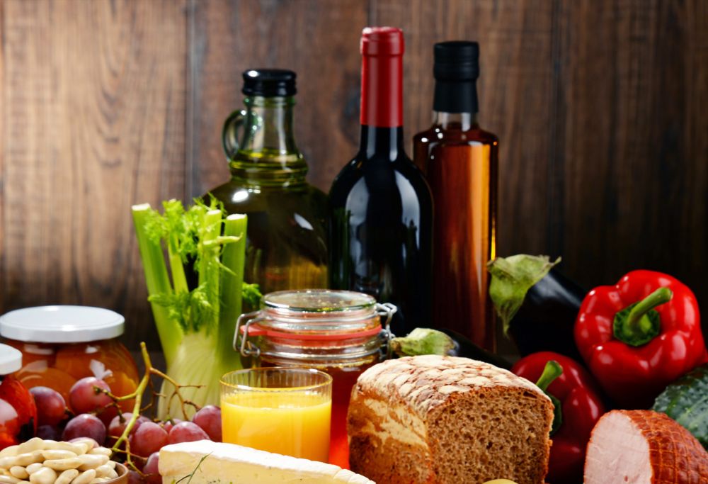 Various food ingredients on a table, including fruits, vegetables, bread, honey and oil. 