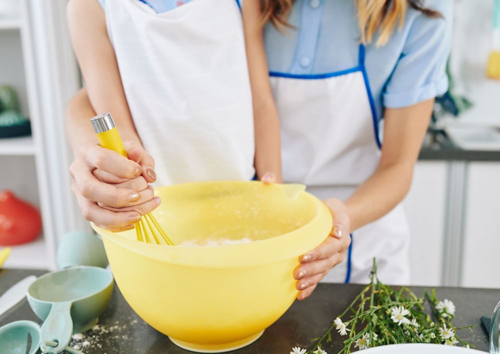 A parent holding a child’s hand as they mix ingredients in a yellow bowl made from Tritan.  
