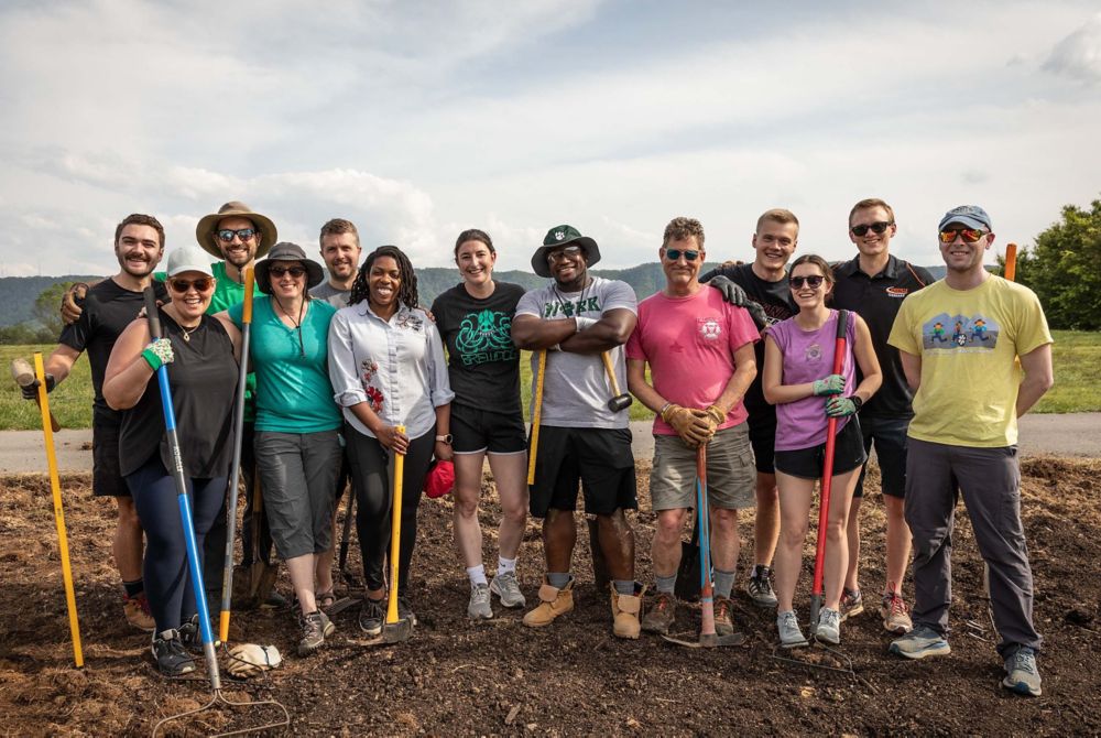 A group of volunteers poses with shovels and rakes. 