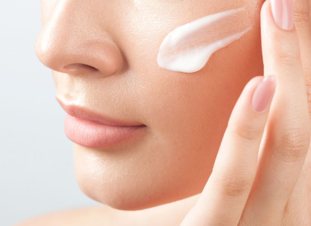 Close-up of a skin care cream being applied by hand to a cheek.   