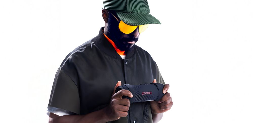 Will.i.am wears sunglasses and a hat while holding the xboom Grab speaker.   