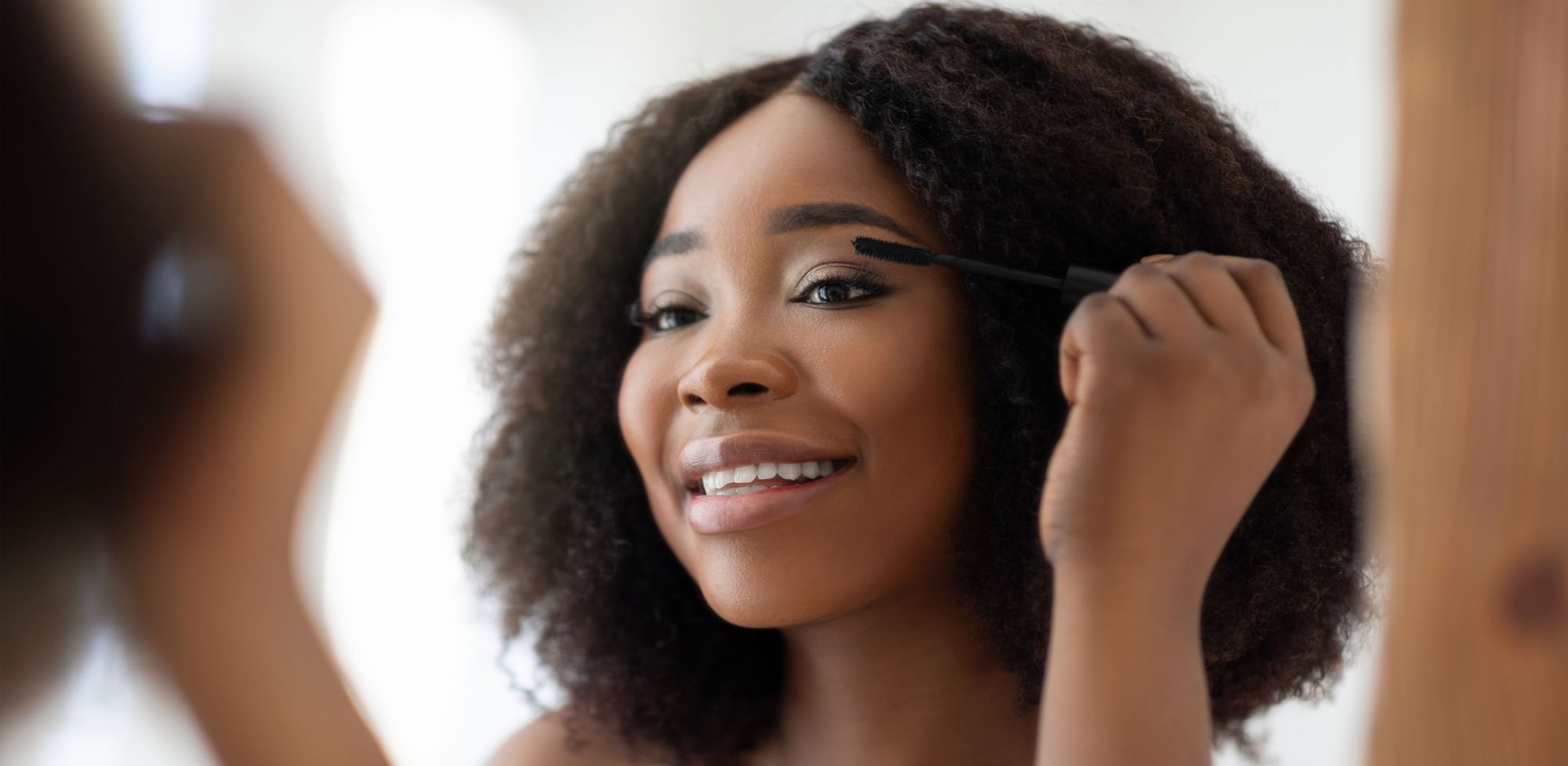A person applies mascara while looking into a mirror. 